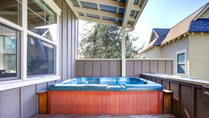 Een houten jacuzzi met een geïntegreerde zitplaats, gelegen onder een overdekte patio met uitzicht op een woongebouw en bomen.