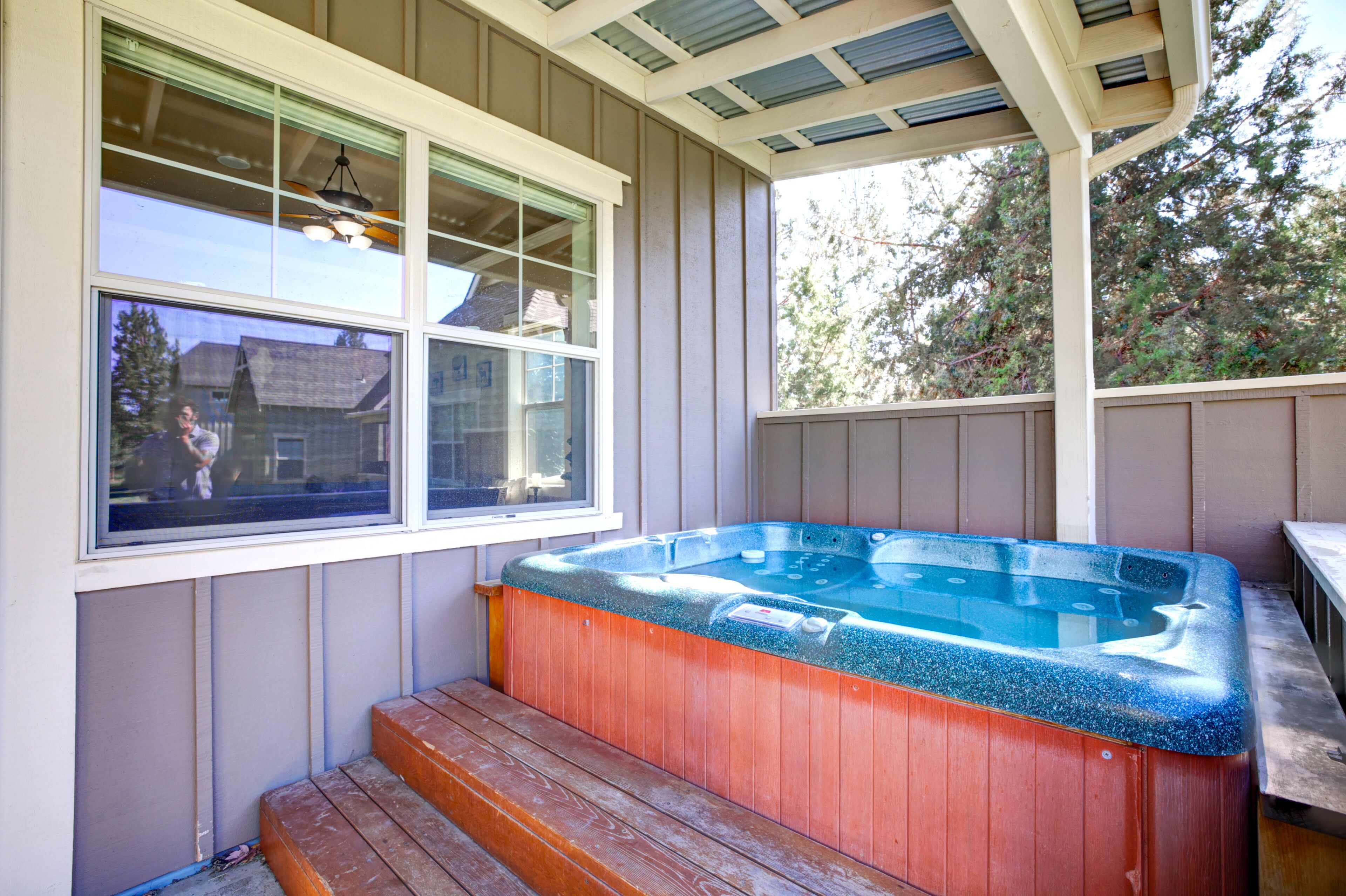 Un bain à remous avec des marches en bois et une fenêtre donnant sur une maison et des arbres.