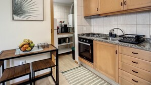 Una cocina moderna con armarios de madera, encimera de granito y pileta de acero inoxidable. Hay una mesa de comedor con sillas y un frutero sobre la encimera.