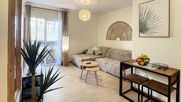 Una sala de estar moderna con un sofá, una mesa redonda y una mesita de centro. Hay una planta grande, una lámpara y una obra de arte colgada en la pared.
