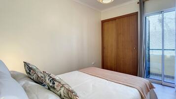 Un dormitorio con una cama, un armario de madera y un ventanal grande.