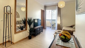 Una sala moderna con un espejo grande, un televisor de pantalla plana, una zona de comedor con mesa y sillas, y un balcón con vistas.