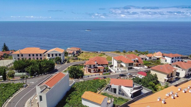 Ein Küstenwohngebiet mit Häusern mit roten Ziegeldächern, freiem Blick auf das Meer und einer Straße, die zum Strand führt.