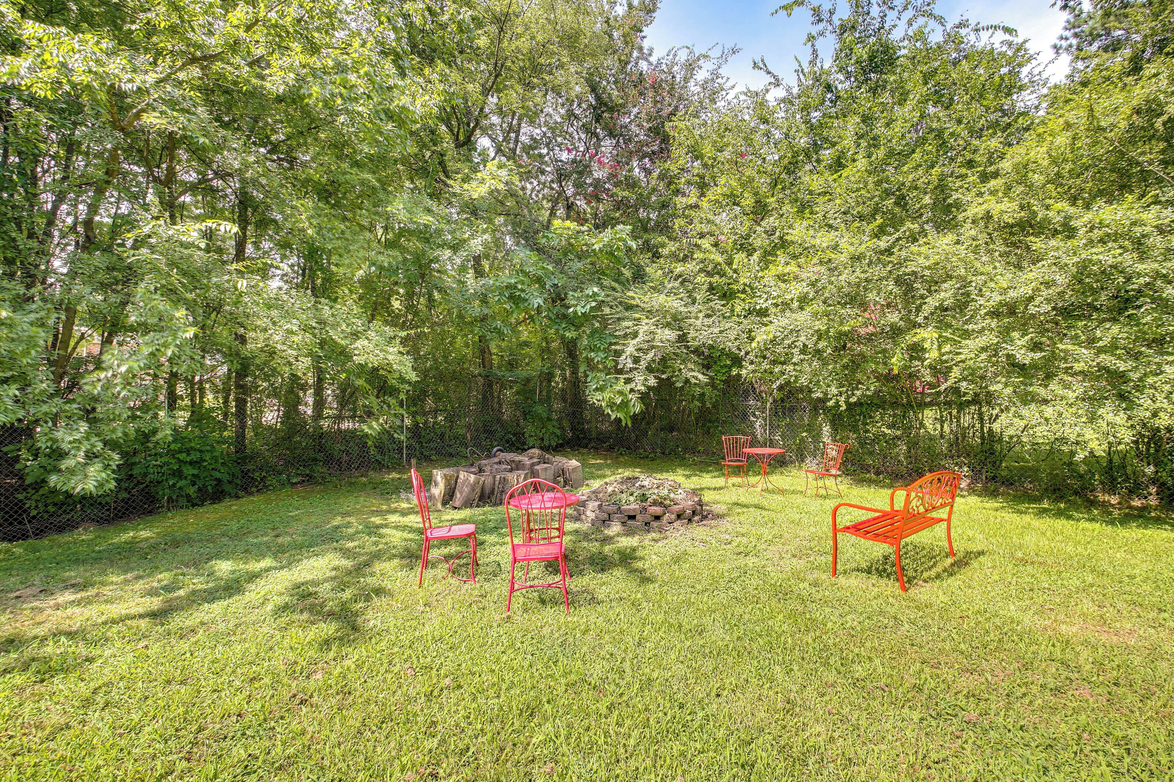 A grassy outdoor area with a stone fire pit, two red metal chairs, and a bench.