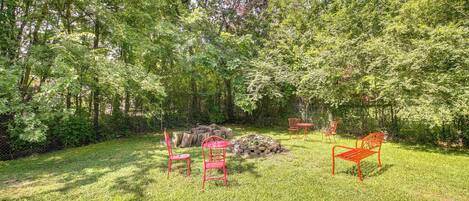 A grassy outdoor area with a stone fire pit, two red metal chairs, and a bench.