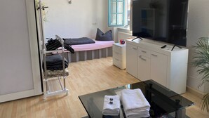 A compact living space with a bed, a TV, a small table with towels, and a wardrobe.