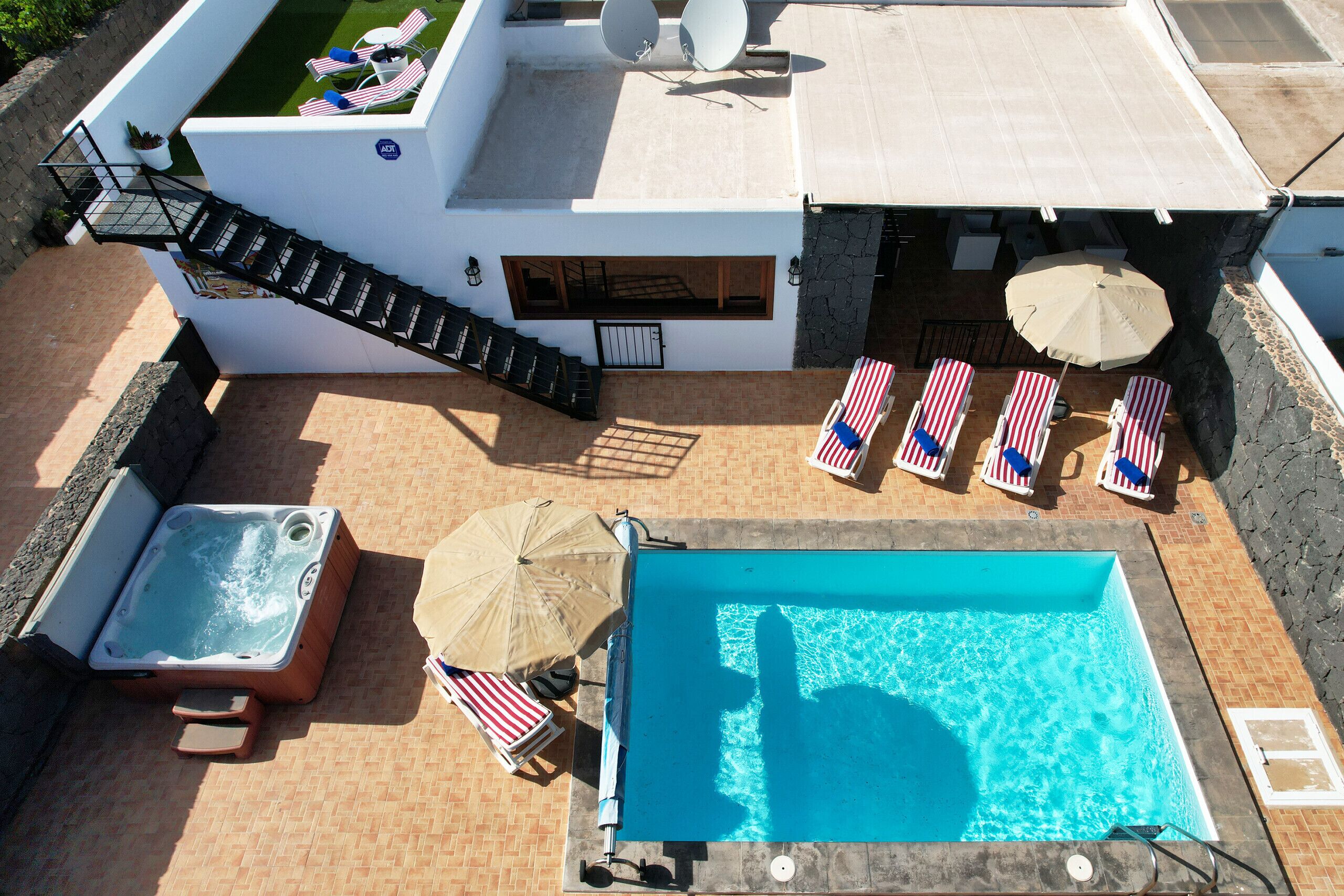 Vista aerea di una zona piscina su un tetto, con vasca idromassaggio, poltrone relax e una scalinata.