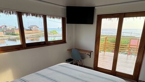 Un dormitorio con cama, escritorio, televisor y ventanas grandes con vistas al mar.