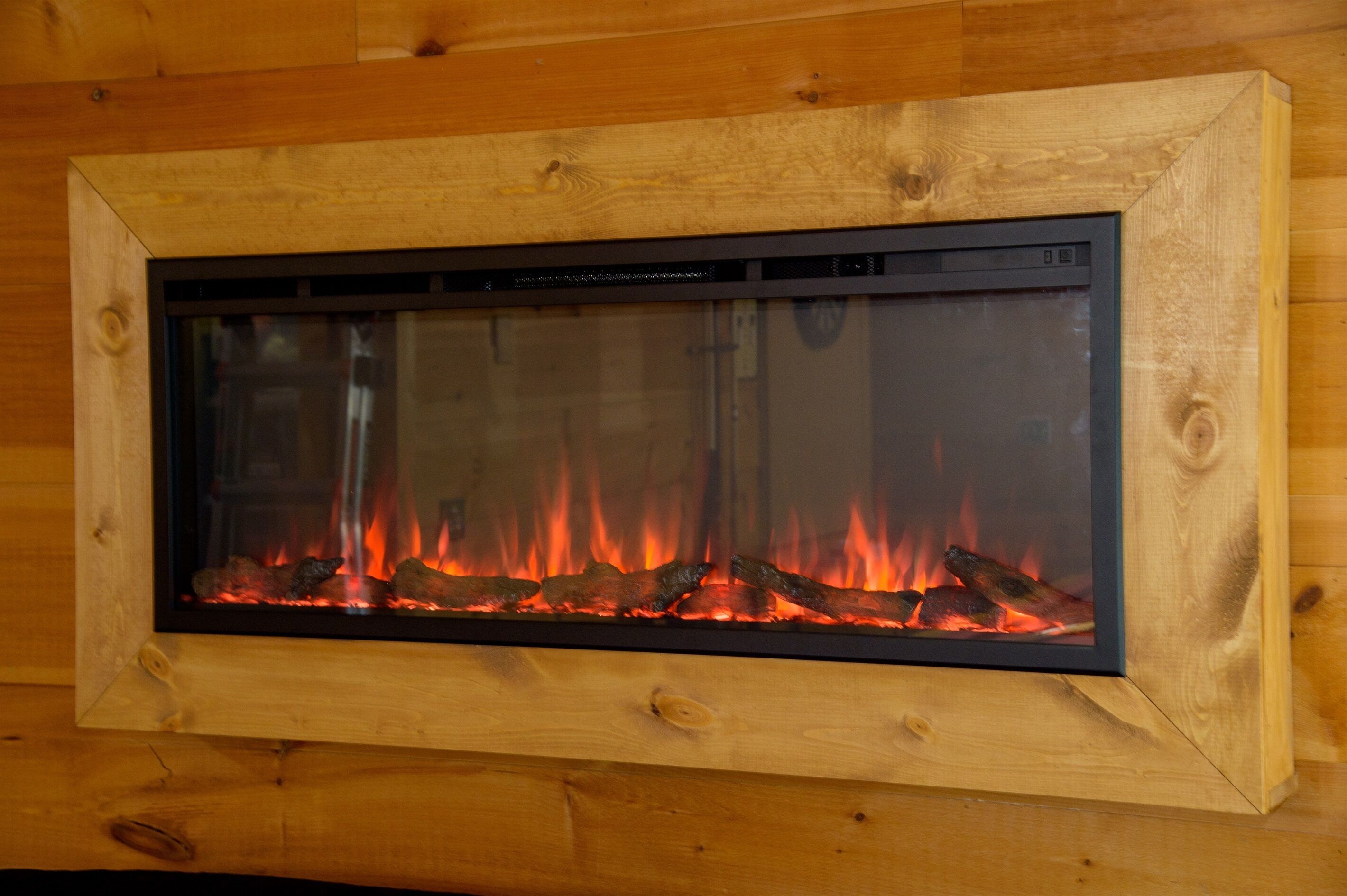 Una chimenea con frente de vidrio, integrada en una pared de madera.