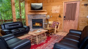 L’intérieur chaleureux d’un chalet avec une cheminée, des canapés en cuir, une table basse en bois et un téléviseur fixé au-dessus de la cheminée.