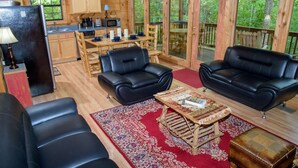 L’intérieur chaleureux d’un chalet comprend un coin repas, deux canapés en cuir noir, une table basse en bois et un tapis rouge à motifs.
