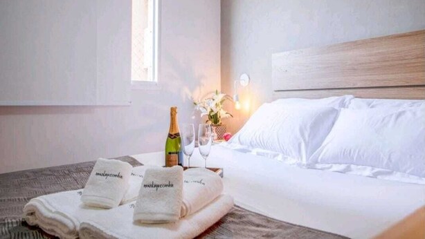 A hotel room with a neatly made bed, a bottle of champagne, two glasses, and a bouquet of flowers. - Apartment 5 guests Santo André near AV Estado Prox Shopping (Utinga Santo André)