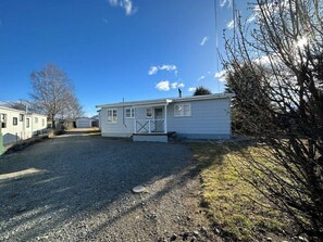 A single-story mobile home with a front porch, a gravel driveway, and a clear blue sky.