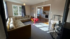 A living room with a sofa, a table, and a fireplace. There is a kitchen visible through an open doorway. - Bach Bliss, Twizel. Free Wifi. (Twizel)