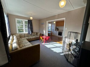 A living room with a sofa, a table, and a fireplace. There is a kitchen visible through an open doorway.