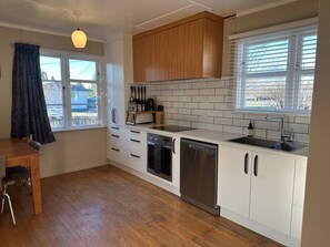 A modern kitchen with white cabinetry, a built-in oven, a dishwasher, and a window with blinds.