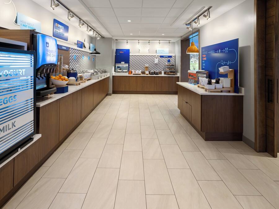 A modern café with a clean, minimalist design, featuring a central counter with various food items and a digital display for yogurt and milk.
