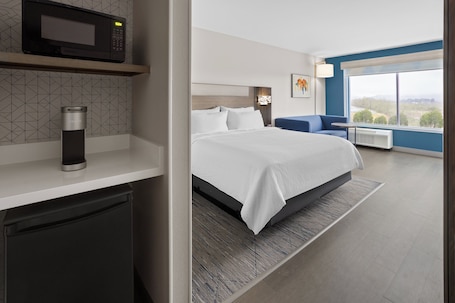 A hotel room with a bed, a microwave, a coffee maker, a small table, and a large window with a view.. Holiday Inn Express & Suites Waynesboro East by IHG