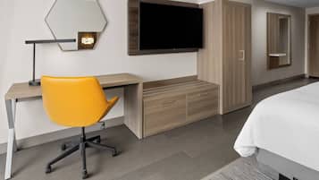 A modern hotel room with a wooden desk, a yellow chair, a large bed, and a flat-screen TV mounted on the wall.