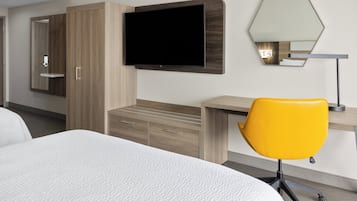 Una habitación de hotel con una cama, un escritorio, una silla, un televisor y un espejo.