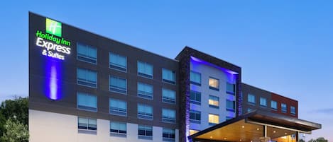 Un edificio de Holiday Inn Express & Suites con un diseño moderno, que cuenta con una entrada amplia y un estacionamiento.
