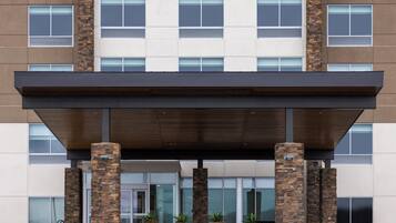 A multi-story building with a modern architectural design, featuring a flat roof, large windows, and stone pillars.