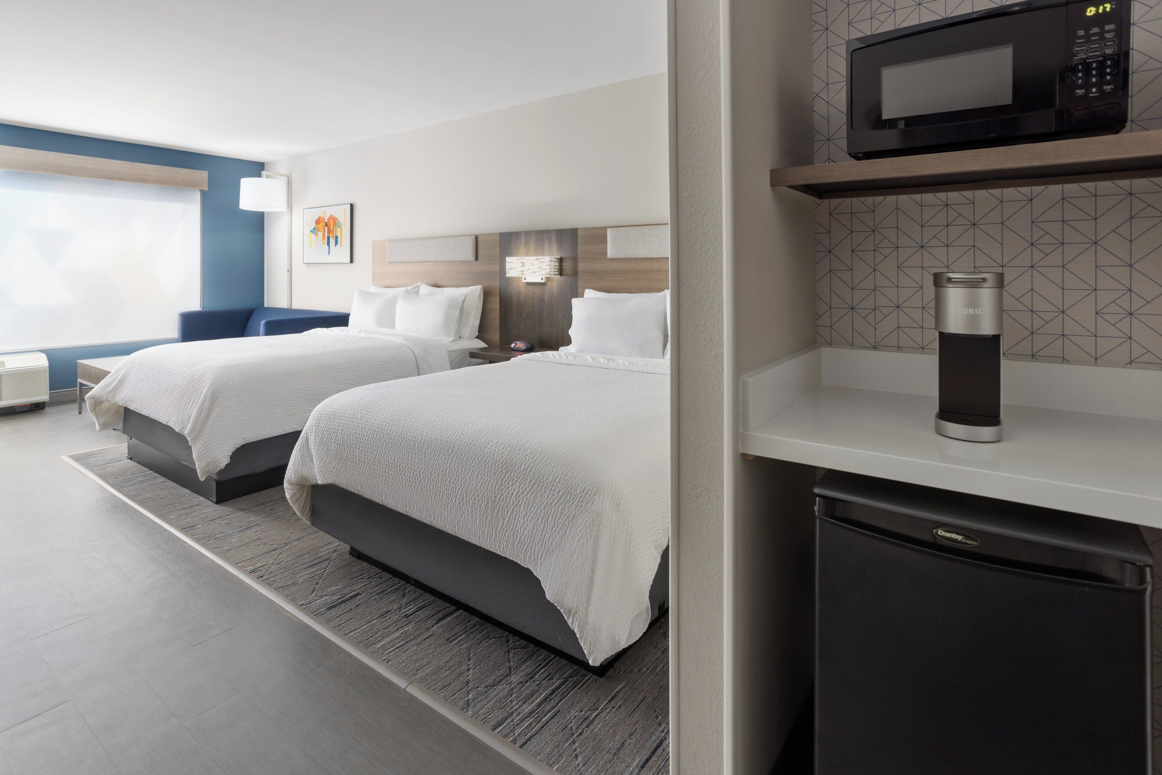 A hotel room with two beds, a microwave, a coffee maker, and a compact refrigerator.