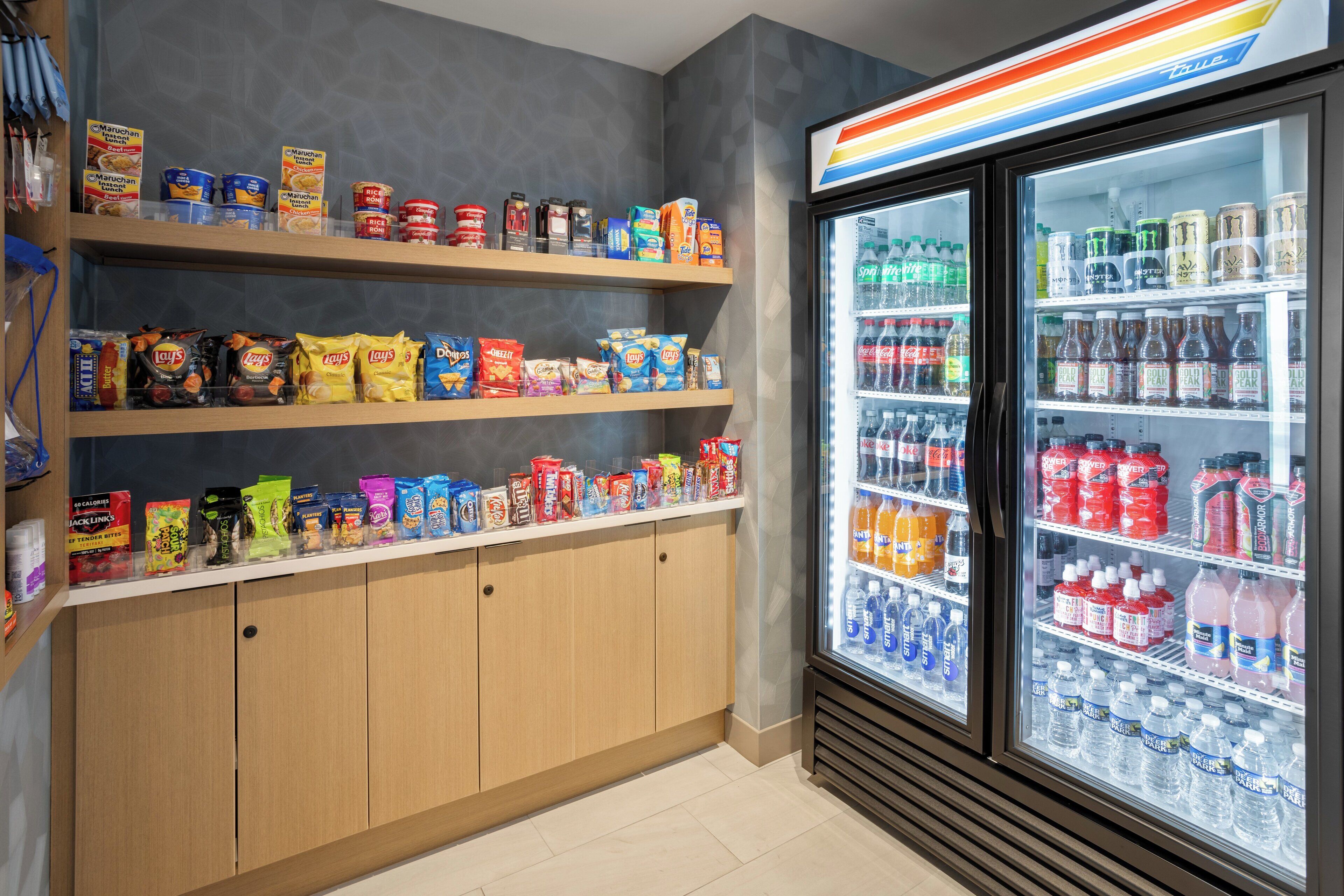 Zona de exhibición de aperitivos y bebidas, con estantes de papas fritas, bocadillos y una sección refrigerada con bebidas embotelladas.