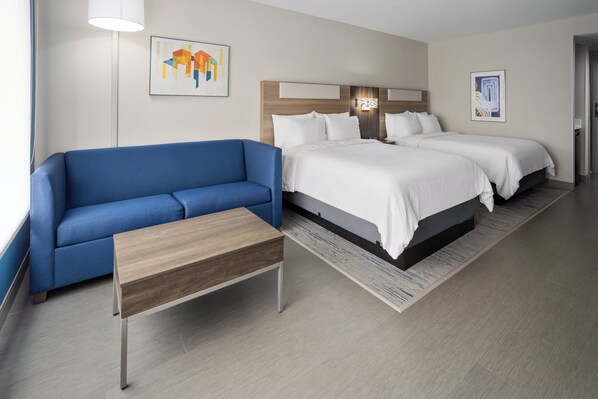 Une chambre d’hôtel avec un canapé bleu, une table d’appoint en bois, un lit double avec une literie blanche et deux appliques murales.