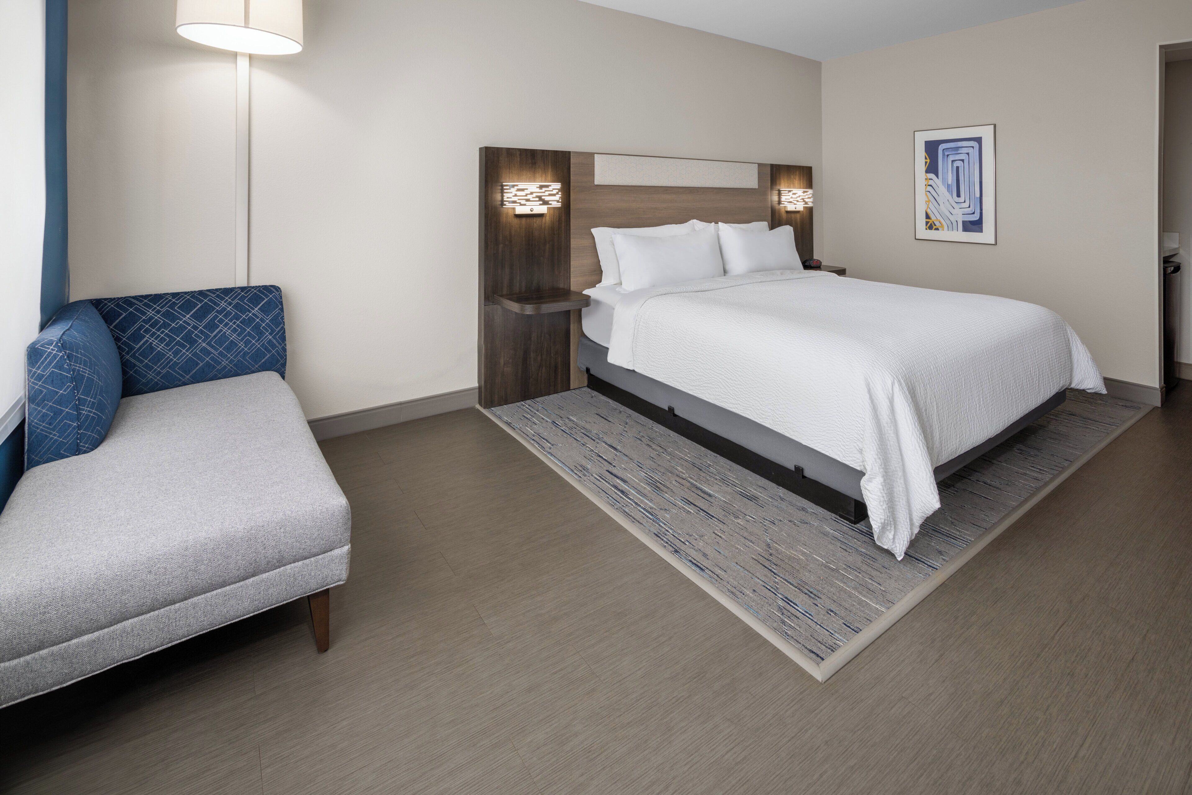 A modern hotel room with a large bed, a seating area, and a wall-mounted light fixture.