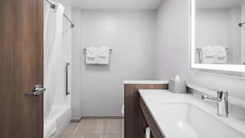 Un baño moderno con tocador de madera, un espejo grande, bañera y ducha.
