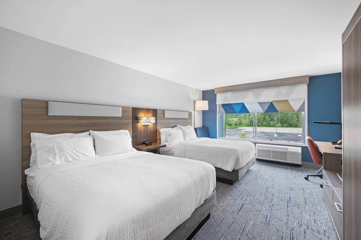 Une chambre d’hôtel avec deux lits, un bureau et une chaise. Il y a une fenêtre donnant sur un paysage verdoyant.