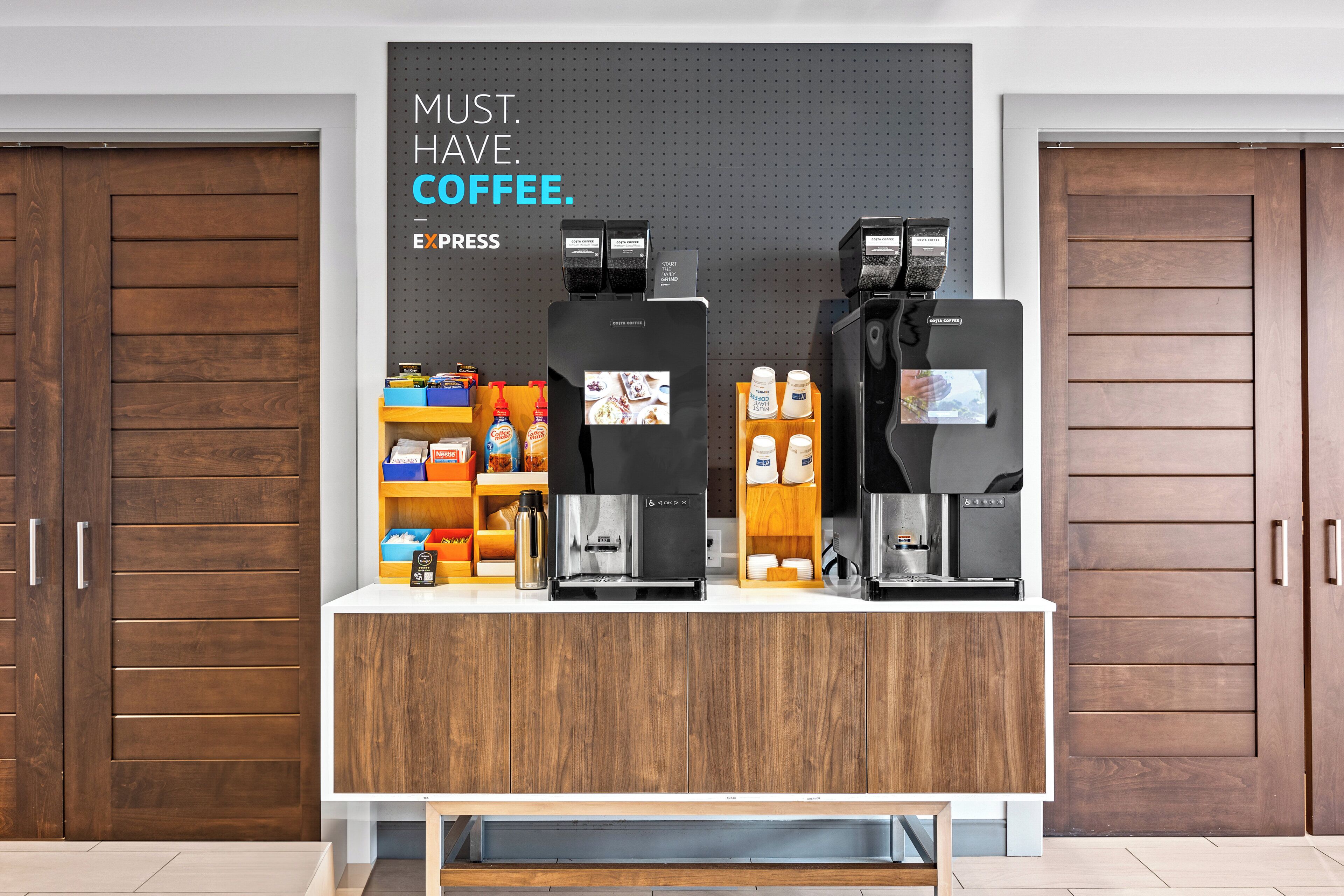 A coffee station with two espresso machines, a coffee press, and various coffee-related items on shelves.