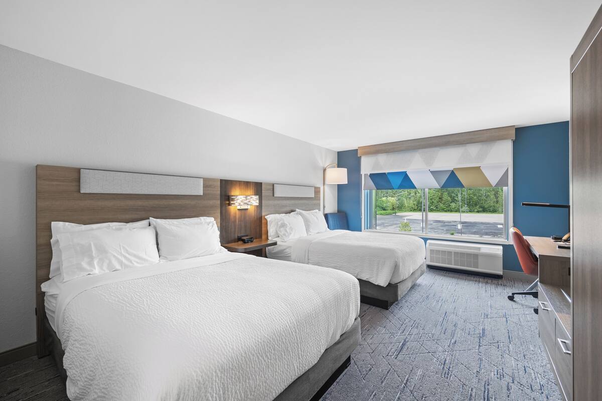 Une chambre d’hôtel avec deux lits, un bureau, une chaise, une fenêtre donnant sur un beau paysage et une lampe fixée au mur.
