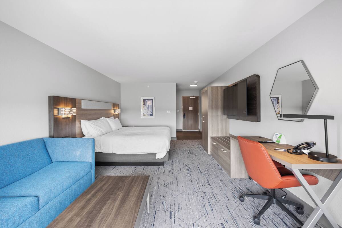 Une chambre d’hôtel avec un lit, un canapé bleu, un bureau avec une chaise, une télévision et un miroir.