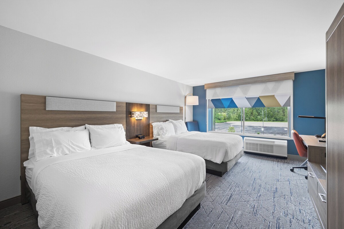 Une chambre d’hôtel avec deux lits, un bureau et une chaise. Il y a une fenêtre donnant sur un paysage verdoyant.