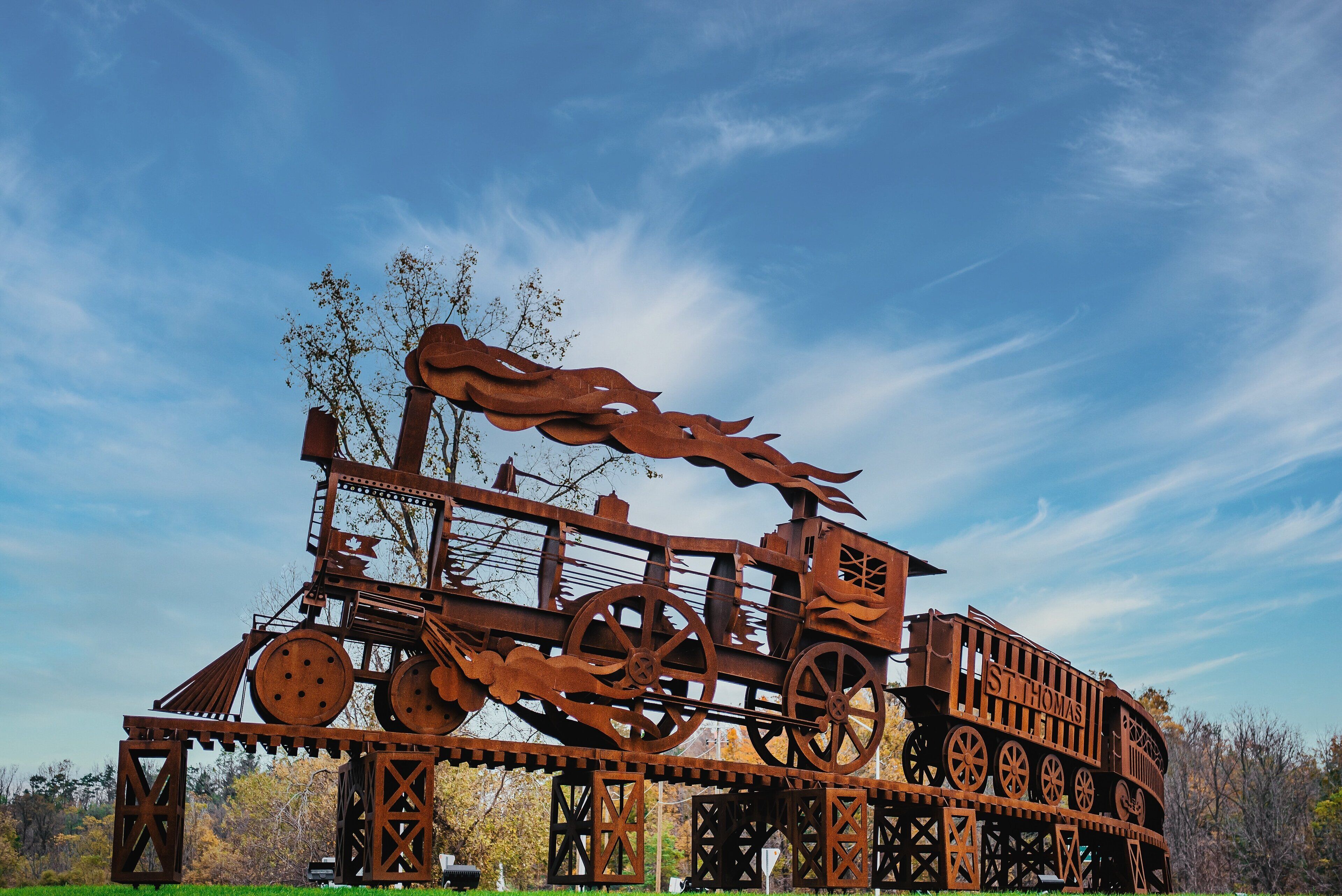 A large metal sculpture of a train with wheels and a dragon head, set against a clear blue sky.