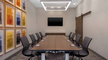A conference room with a long table, chairs, a flat-screen TV, and framed artwork on the wall.