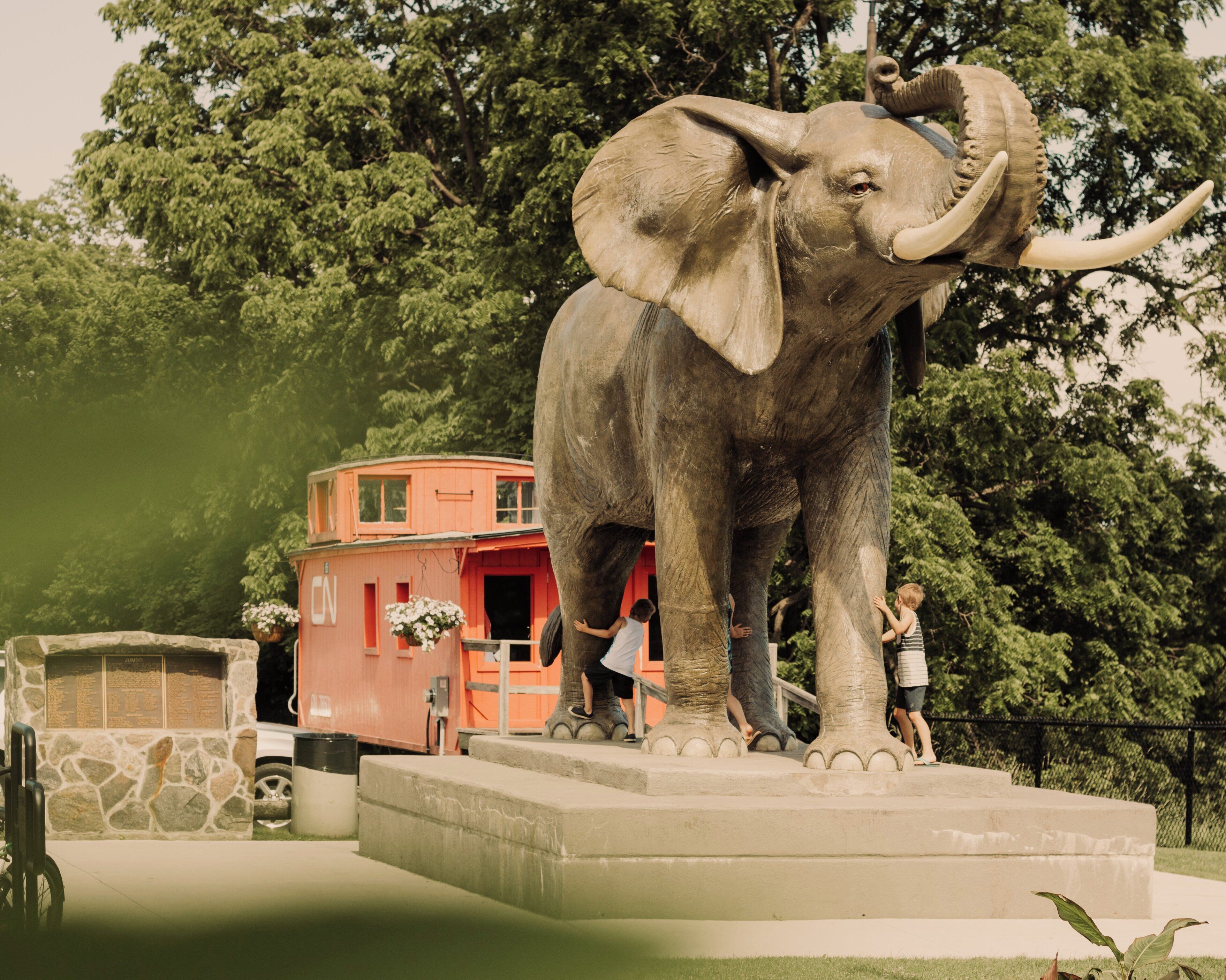 A large elephant statue on a pedestal with a small building in the background.