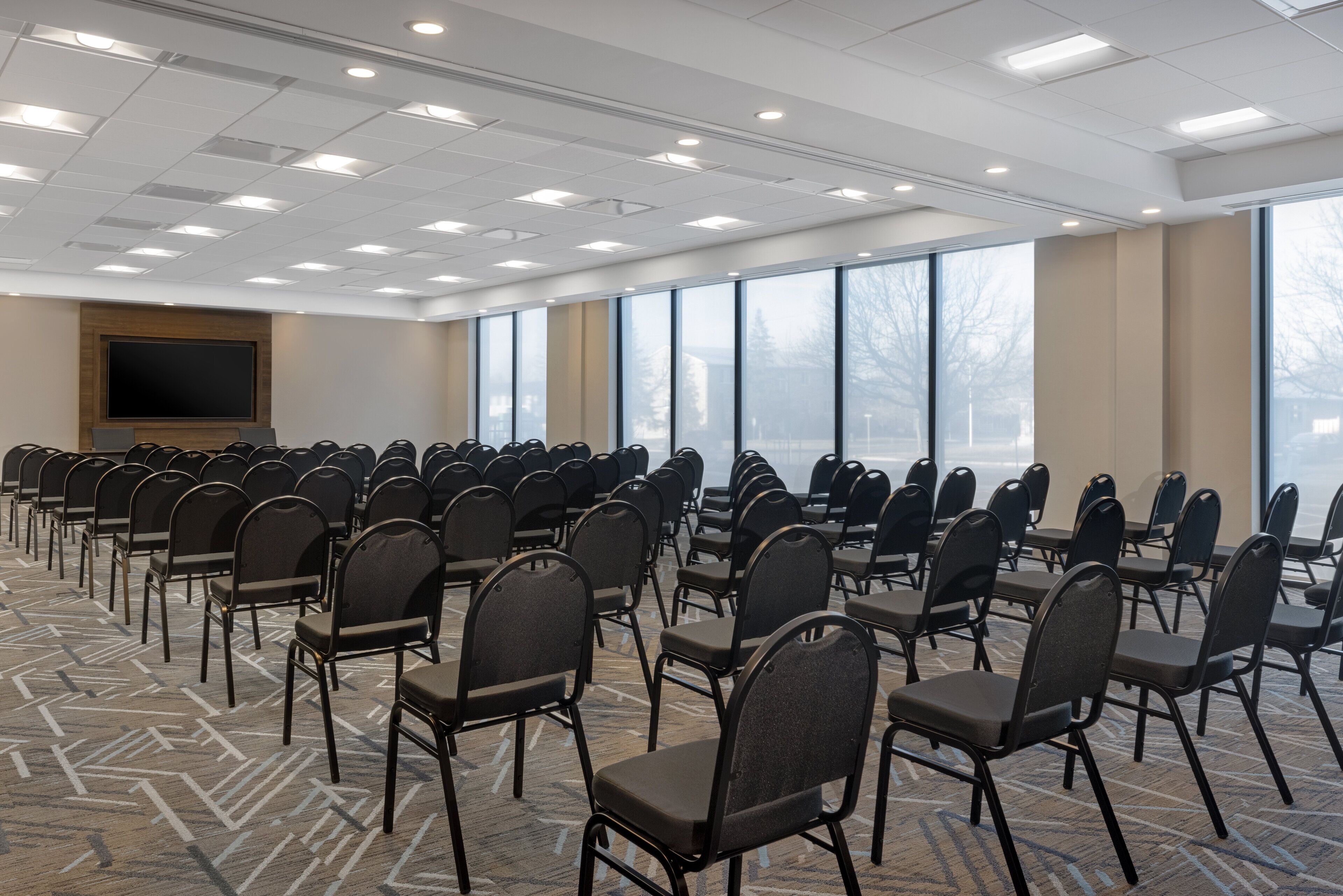 A conference room with rows of chairs, a large screen, and large windows.