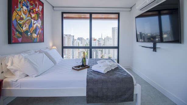 Une chambre d’hôtel moderne avec un grand lit, une vue sur la ville, une peinture abstraite aux couleurs vives et un téléviseur fixé au mur.