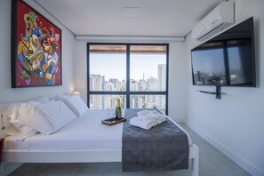 Ein modernes Hotelzimmer mit einem großen Bett, Blick auf die Stadt, einem farbenfrohen abstrakten Gemälde und einem wandmontierten Fernseher.