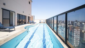 Une piscine à débordement offrant une vue sur la ville, des chaises longues et une façade de bâtiment moderne.