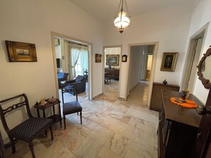A spacious living area with a marble floor, a dining table with chairs, a sofa, and a chandelier.