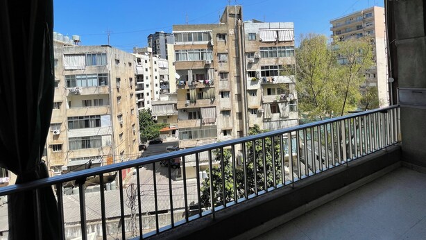 A balcony with a view of multi-story residential buildings, a street, and some greenery. - New Jdeideh, Including Generator, Furnished Apartment, Parking, Great Location (Jdeideh)