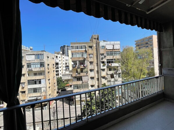 A balcony with a view of multi-story residential buildings, a street, and some greenery.
