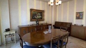A dining room with a round wooden table, blue upholstered chairs, a chandelier, and striped wallpaper. - New Jdeideh, Including Generator, Furnished Apartment, Parking, Great Location (Jdeideh)