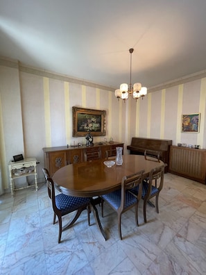 A dining room with a round wooden table, blue upholstered chairs, a chandelier, and striped wallpaper.