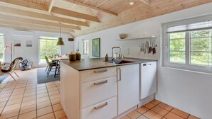 A modern kitchen with white cabinetry, a central island, and a window with a view of greenery. - "Osmo" - 900m from the sea by Interhome (Ulfborg)