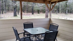 Un patio cubierto con una mesa y sillas de metal, rodeado de vigas de madera y vistas a un bosque.